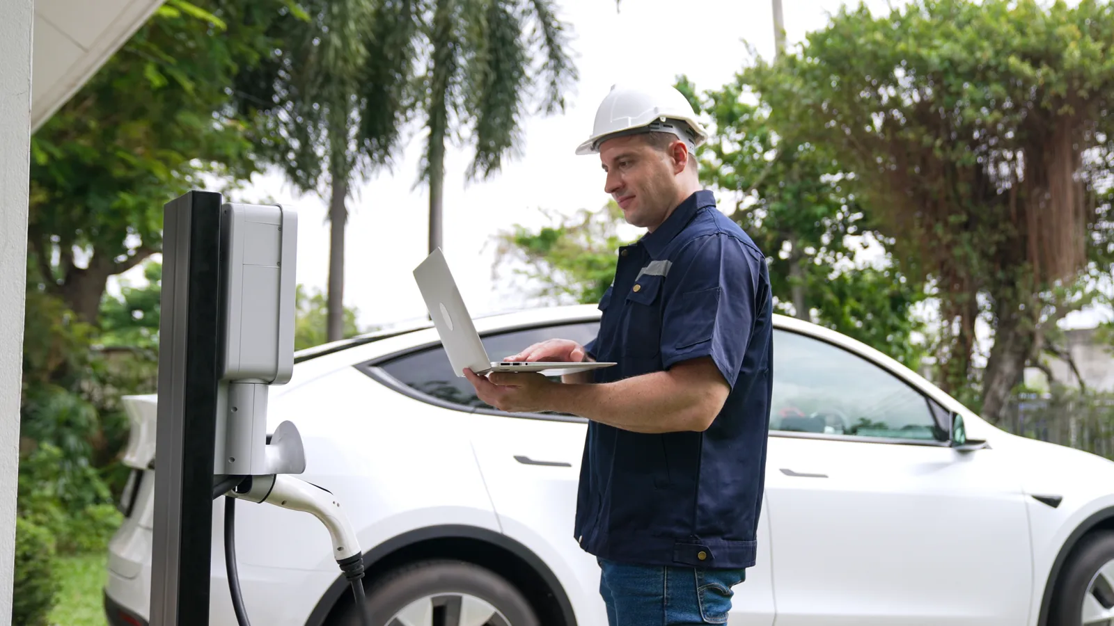 Electrician installing and inspecting an EV charger at home with a white electric vehicle in the background, representing different types of EV chargers.